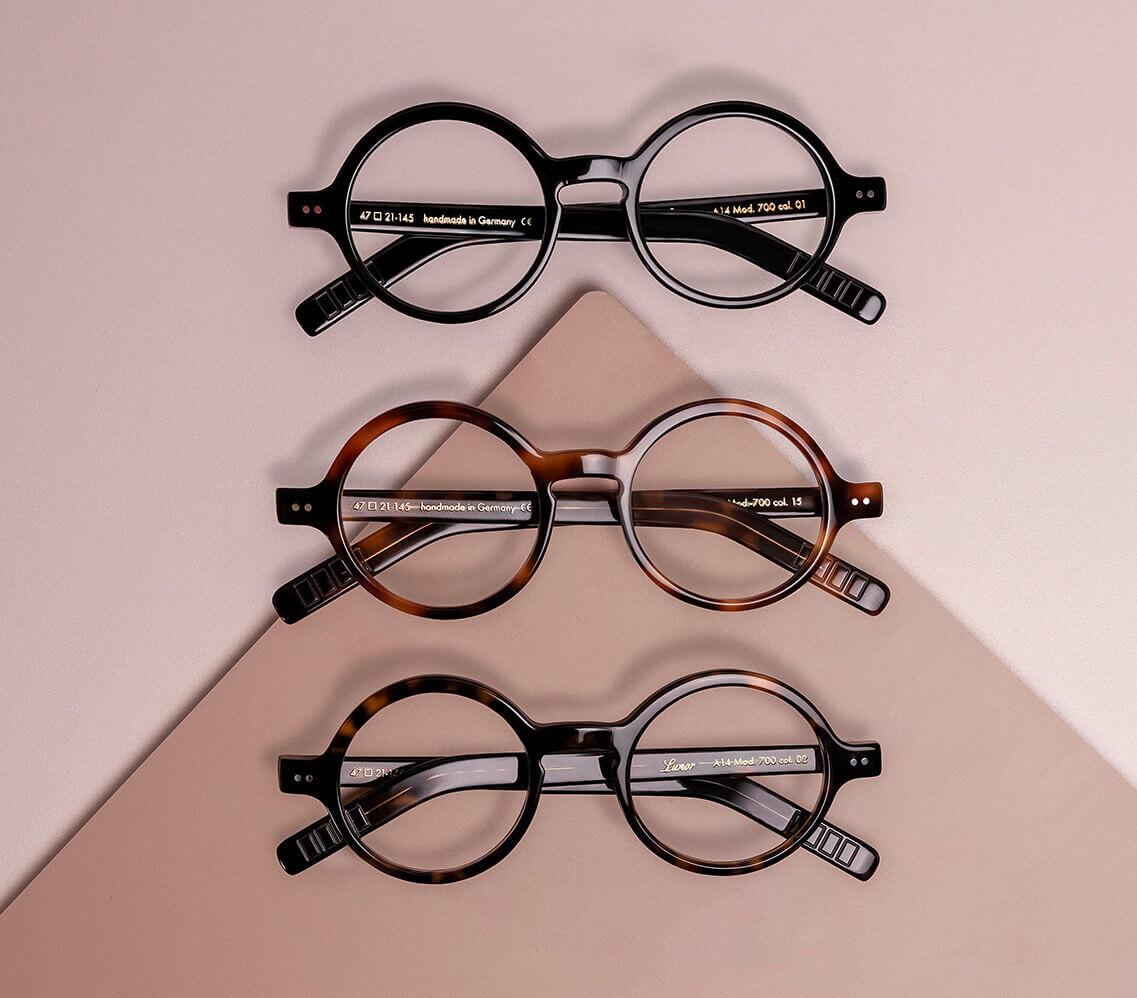 drei lunor korrektionsbrillen werden auf einem warmen hintergrund untereinander dargestellt